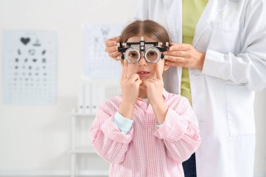 Female ophthalmologist putting trial frame on little girl in clinic