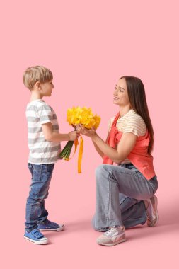 Son greeting his happy mother with bouquet of beautiful narcissus on pink background