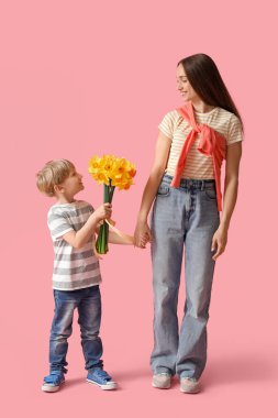 Happy woman and her little son with bouquet of beautiful narcissus on pink background