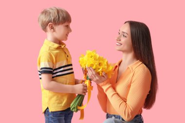 Son greeting his happy mother with bouquet of beautiful narcissus on pink background
