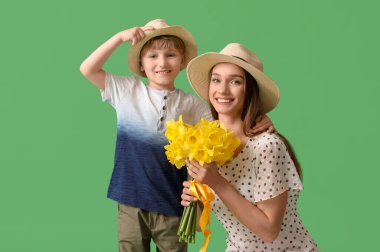 Happy woman and her little son with bouquet of beautiful narcissus on green background