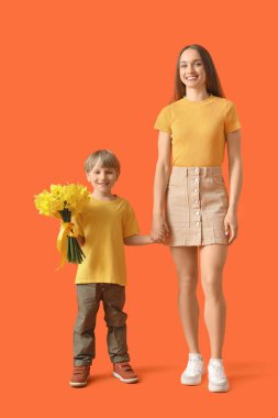 Happy woman and her little son with bouquet of beautiful narcissus on orange background
