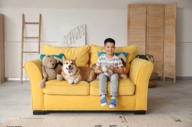 Little happy Asian boy with cute Corgi dog and toys sitting on sofa at home