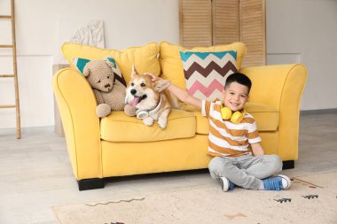 Little happy Asian boy with cute Corgi dog in headphones sitting at home
