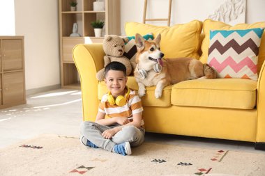 Little happy Asian boy with cute Corgi dog in headphones sitting at home