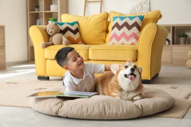 Little happy Asian boy reading book with cute Corgi dog at home