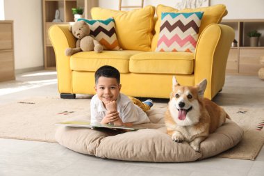 Little happy Asian boy reading book with cute Corgi dog at home