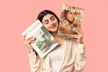 Beautiful young happy woman with magazines on pink background