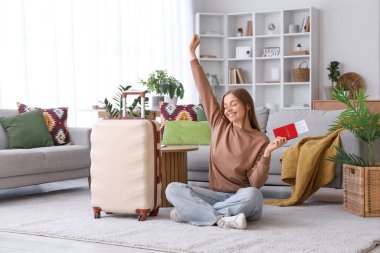 Female tourist with passport and suitcase sitting on floor at home