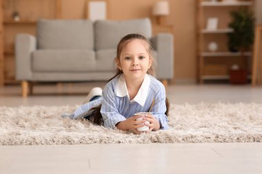 Cute little girl with spoon and yogurt lying on floor at home