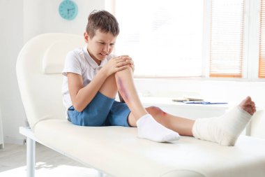 Little boy with injured leg sitting on couch in clinic