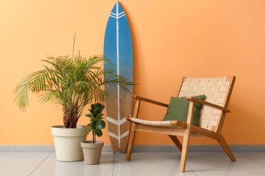 Sarı duvarın yanında bitki ve koltuk olan sörf tahtası.