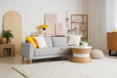 Interior of cozy living room with sofa, coffee table and shelving unit near white brick wall