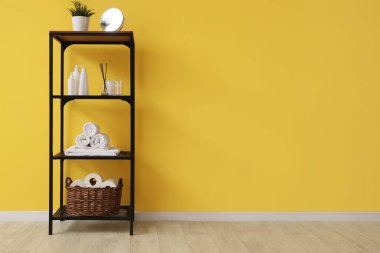 Sarı duvarın yanında banyo aksesuarları olan raflar.