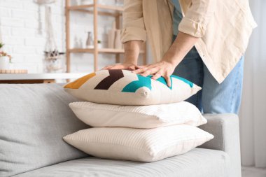 Young man adjusting sofa cushions at home, closeup