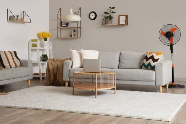 Interior of stylish living room with floor electric fan and laptop