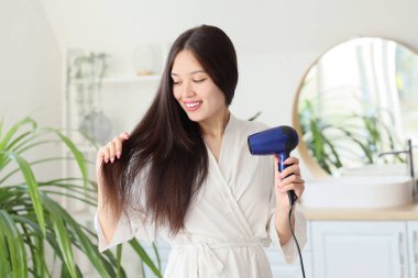 Young Asian woman drying hair in bathroom