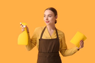Young woman with spray bottle and rag on orange background