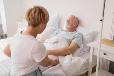 Sick mature man with infusion drip and his wife in bedroom