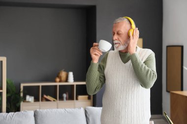 Mature man in headphones drinking coffee at home