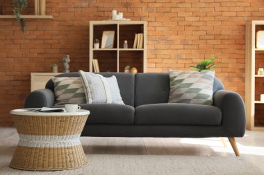 Oturma odasının içinde siyah kanepe ve rattan masa var.