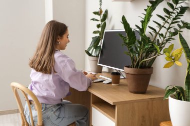 Young woman working with computer and plants at table in office