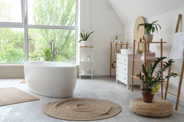 İçinde seramik küvet ve bitkiler olan hafif bir banyo.