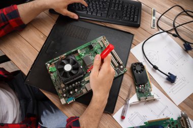 Male technician repairing computer board at table in service center, closeup