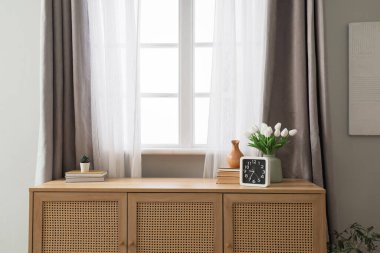 Vase with tulips, clock and books on commode in living room