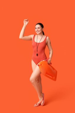 Female lifeguard with rescue buoy waving hand on orange background