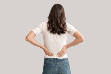 Beautiful young woman suffering from back pain on grey background