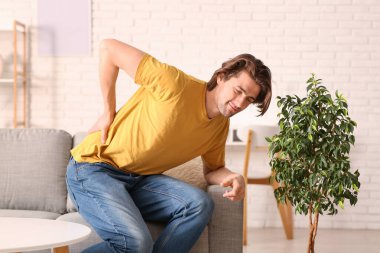 Handsome young man sitting on sofa and suffering from back pain at home