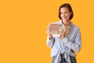 Beautiful young happy woman with lunchbox of tasty food on yellow background