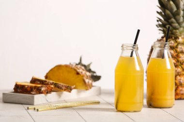 Taze olgun ananas ve beyaz duvarın yanındaki fayans masasında lezzetli meyve suyu şişeleri.