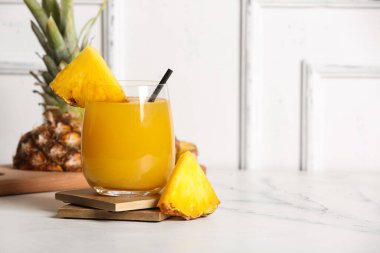 Beyaz ahşap duvarın yanındaki masada bir bardak taze ananas suyu.