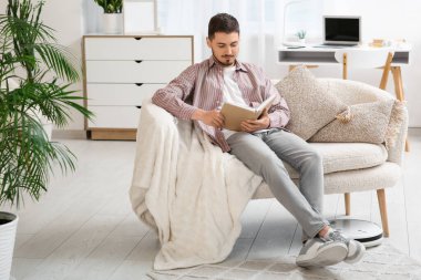 Modern robot vacuum cleaner near sofa with resting young man at home