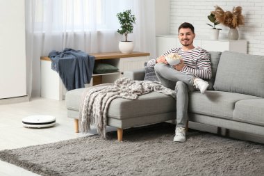 Young man watching movie with modern robot vacuum cleaner at home