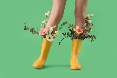 Woman with flowers in gumboots on green background, closeup