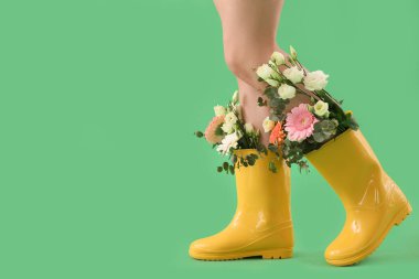Woman with flowers in gumboots on green background, closeup
