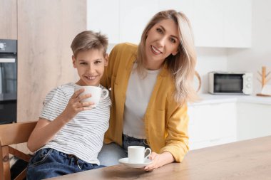 Little boy and his mother drinking in kitchen