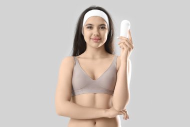 Young woman with deodorant on light background