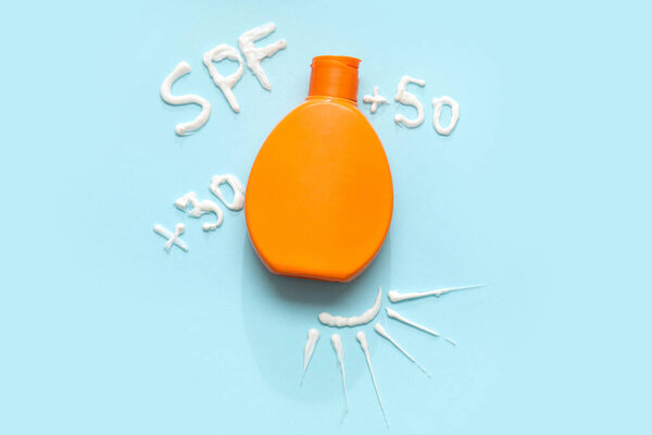 Bottle of sunscreen and word SPF written with cream on color background