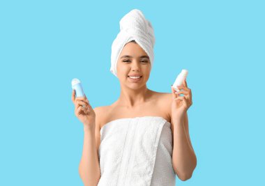 Young woman in towel with deodorants on blue background