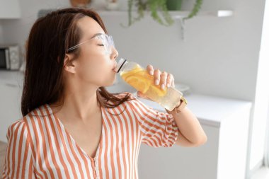 Young Asian woman drinking lemon water in kitchen, closeup