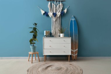 Interior of stylish room with tapestry, commode and surfboard