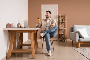 Young man with bottle of lemon water sitting at table in office
