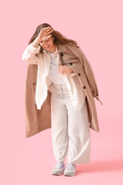 Young woman in trench coat with strong wind on pink background
