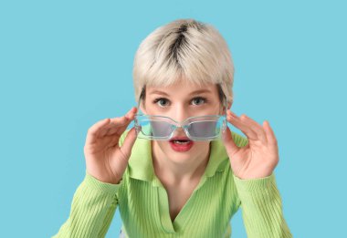 Portrait of surprised young woman with sunglasses on blue background
