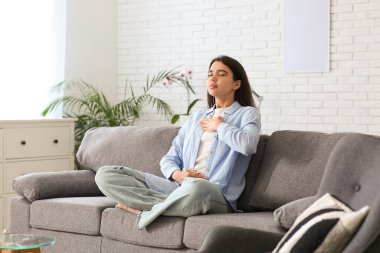 Beautiful young woman doing breath practice on sofa at home