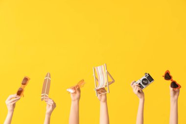 Female hands with stylish sunglasses, mini deck chair, surfboard and photo camera on yellow background
